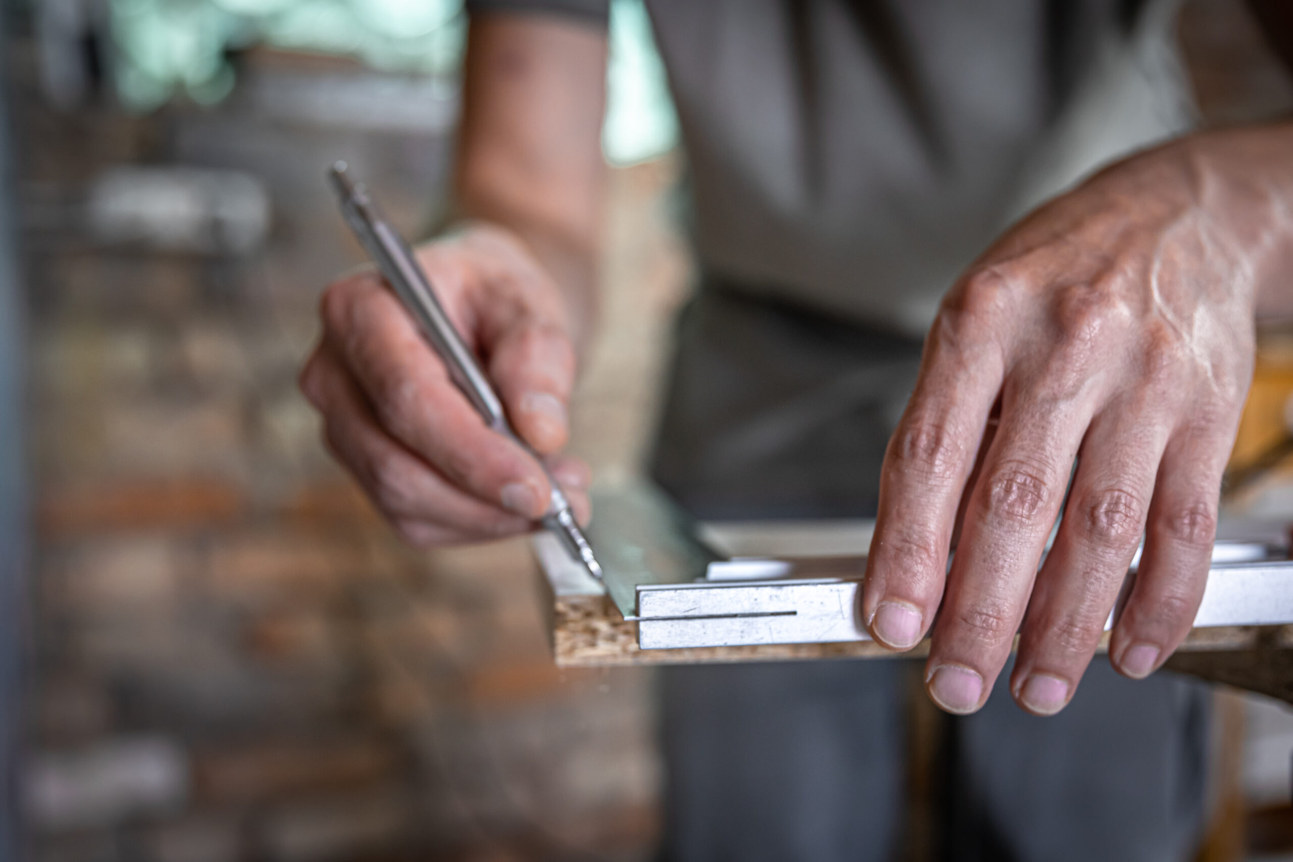 the carpenter marks the piece of wood with a pen and ruler.